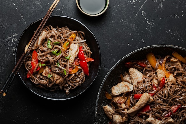 Tigela com frango asiático frito macarrão soba com vegetais em um fundo de pedra preto escuro de cima, prato de macarrão chinês tailandês ou japonês com molho de soja