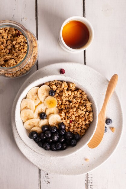 Tigela com granola saudável com mel, banana e frutas vermelhas no café da manhã