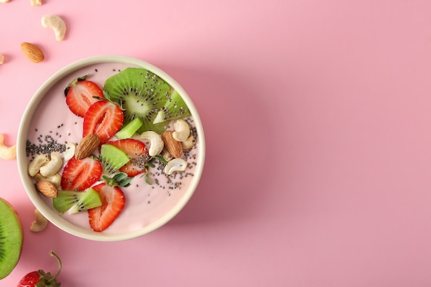 Tigela com iogurte rosa e frutas frescas na superfície colorida