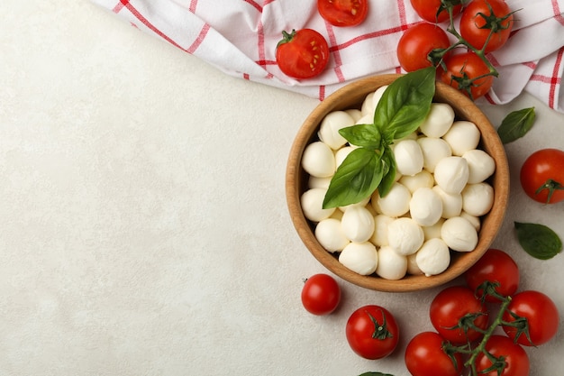 Tigela com mussarela e manjericão, tomate e toalha no fundo texturizado branco, espaço para texto