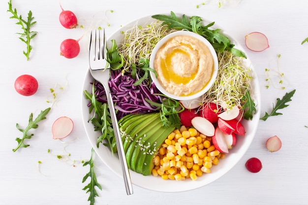 Tigela de almoço de milho doce de abacate vegan com hummus, repolho roxo, rabanete e brotos