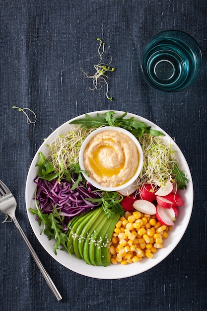 Tigela de almoço de milho doce de abacate vegan com hummus, repolho roxo, rabanete e brotos