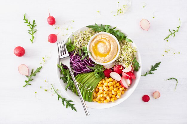 Tigela de almoço de milho doce de abacate vegan com hummus, repolho roxo, rabanete e brotos