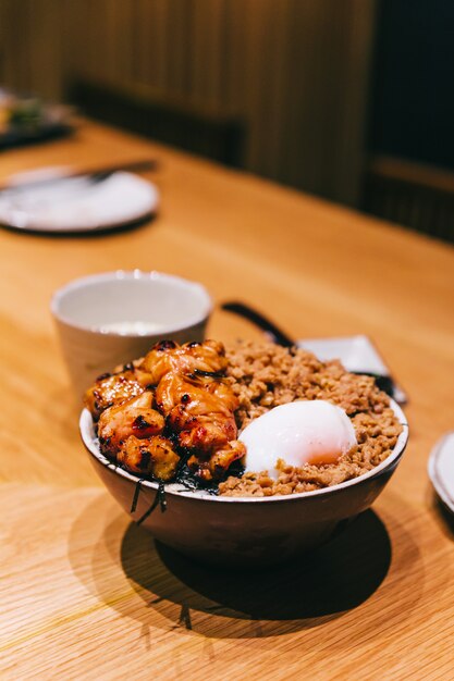 Tigela de arroz Yakitori de frango com carne de porco picada servida com ovo cozido no vapor chinês, colher e pauzinhos.