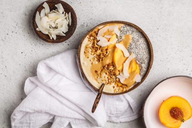 Tigela de batido com pudim de chia, pêssego, coco e granola em uma tigela de coco.