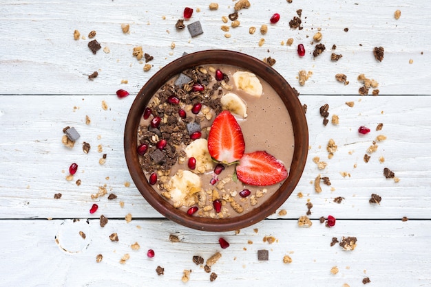 Tigela de batidos de proteína de cacau e banana com sementes de granola de chocolate, morango e romã