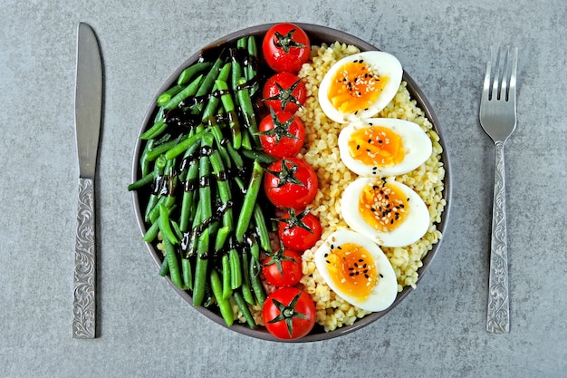 Tigela de Buda com bulgur, feijão verde, tomate cereja e metades de ovo cozido. Comida saudável em uma tigela. O conceito de nutrição dietética.