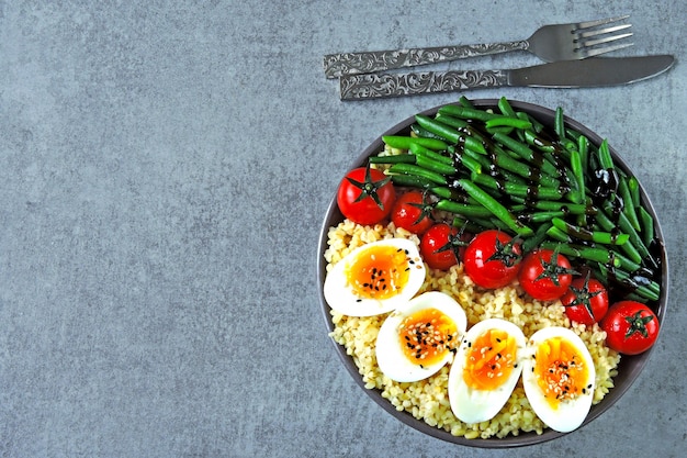 Tigela de Buda com bulgur, feijão verde, tomate cereja e metades de ovo cozido. Comida saudável em uma tigela. O conceito de nutrição dietética.