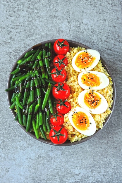 Tigela de Buda com bulgur, feijão verde, tomate cereja e metades de ovo cozido. Comida saudável em uma tigela. O conceito de nutrição dietética.