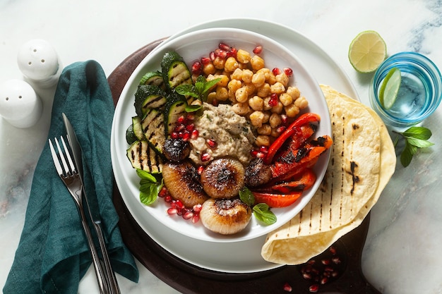 Tigela de Buda mediterrânea italiana com cebola caramelizada Baba ghanoush, grão de bico picante e legumes grelhados, comida vegana saudável e pão pita