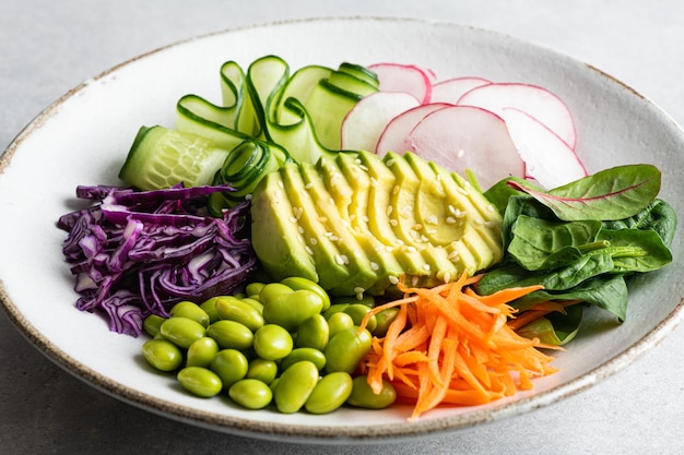 Tigela de Buda vegan com abacate, feijão edamame, pepino, repolho roxo, cenoura, rabanete e espinafre. Salada de vegetais. Comida saudável, vista de cima, foco seletivo