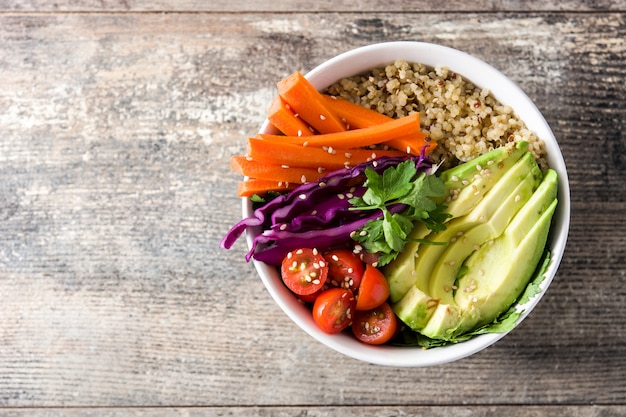 Foto tigela de buda vegan com legumes crus frescos e quinoa na mesa de madeira