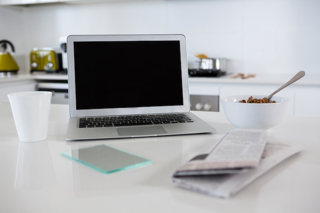 Tigela de café da manhã com caneca de café, laptop e jornal na cozinha