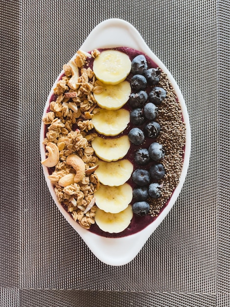 Foto tigela de café da manhã saudável com iogurte, mirtilos, banana, granola e sementes de chia vista de cima