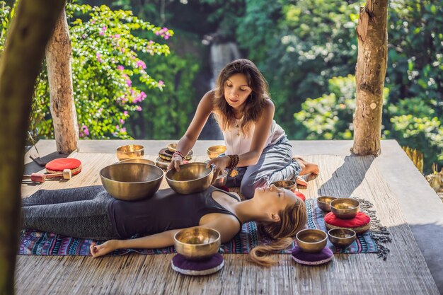 Tigela de canto de cobre de buda do Nepal no salão de spa jovem linda fazendo massagem terapêutica cantando