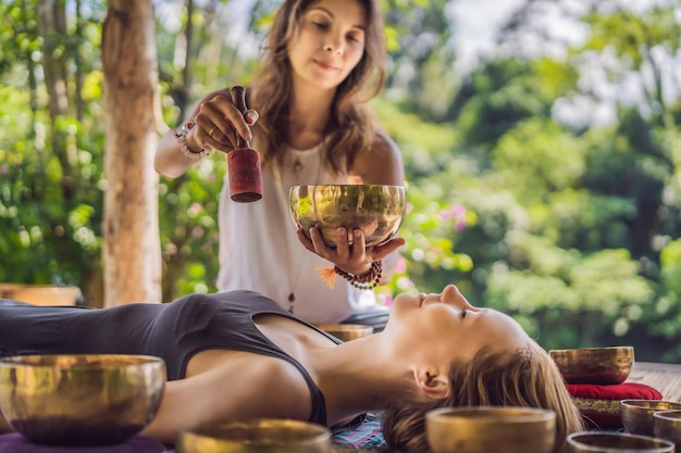 Tigela de canto de cobre de buda do nepal no salão de spa jovem linda fazendo massagem terapêutica cantando