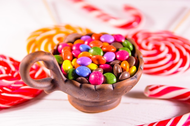 Tigela de cerâmica com doces coloridos e pirulitos em uma mesa de madeira