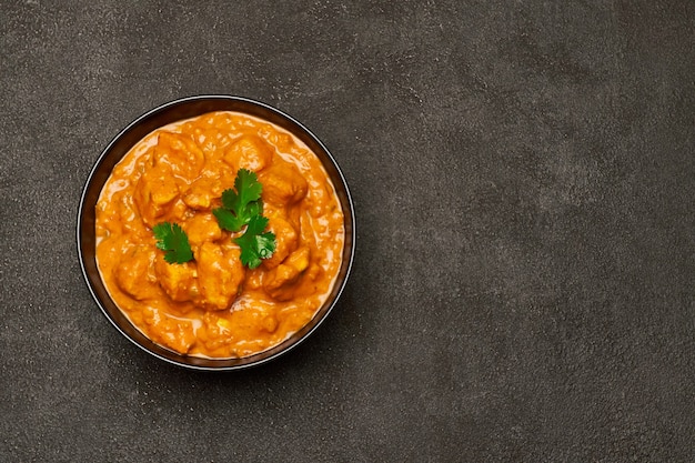 Tigela de cerâmica preta com curry de frango tradicional na mesa escura