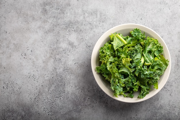 Tigela de couve picada verde fresca em fundo de pedra rústica cinza, vista superior, close-up, copie o espaço. Ingrediente para fazer salada saudável. Conceito de alimentação limpa, desintoxicação ou dieta com espaço para texto