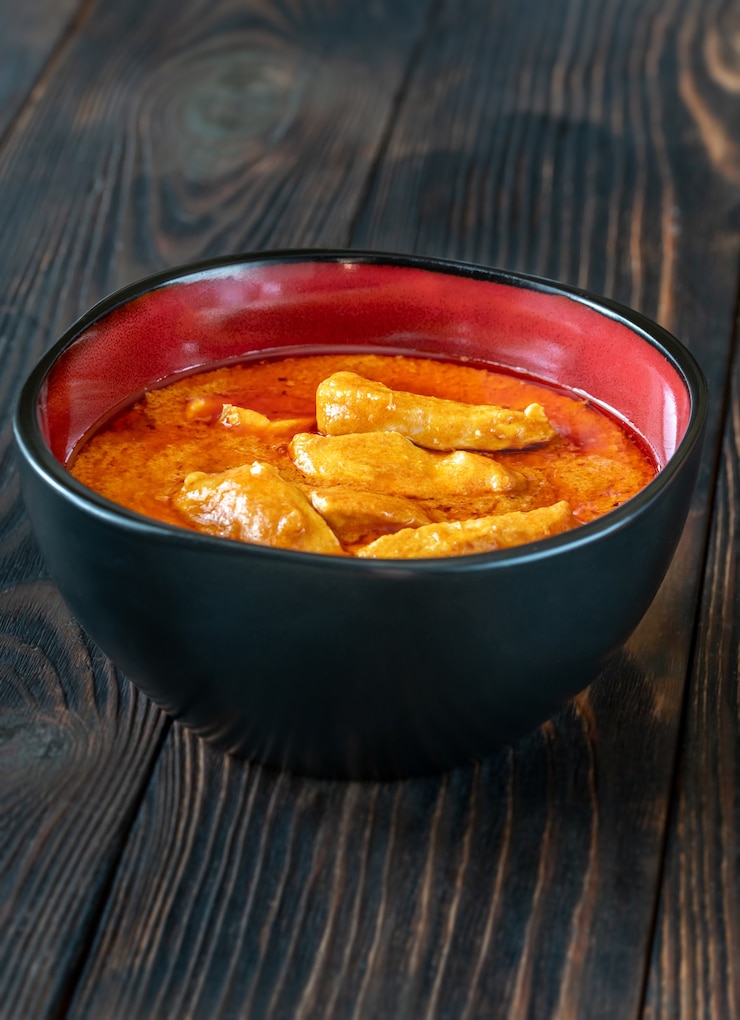Foto tigela de curry de frango vermelho tailandês no fundo de madeira