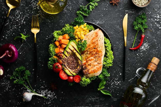 Tigela de dieta filé de frango abacate abóbora tomate cereja linho e milho em uma tigela preta tigela buda vista superior espaço livre para texto