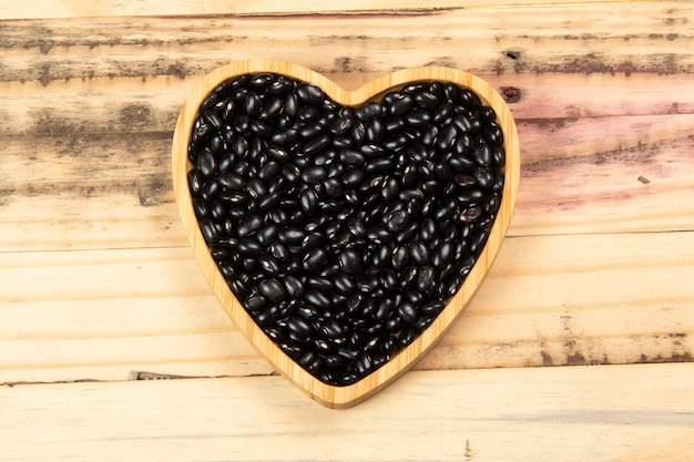 Tigela de feijão preto em forma de coração na mesa de madeira