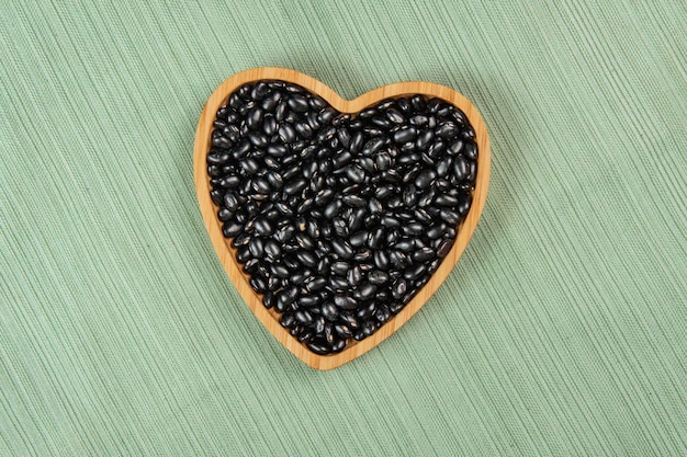 Tigela de feijão preto em forma de coração na toalha de mesa verde