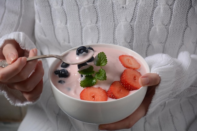 Tigela de frutas frescas misturadas e iogurte com morangos frescos de fazenda e mirtilos nas mãos da menina