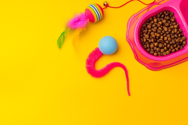 Tigela de gato com comida seca e brinquedos em estúdio de fundo amarelo