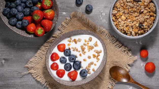 Tigela de granola caseira com iogurte e frutas frescas em fundo de madeira da vista superior