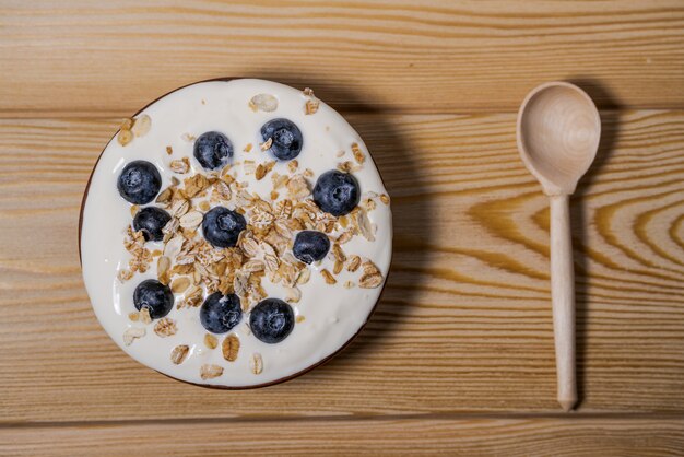 Tigela de granola caseira com iogurte e frutas frescas em fundo de madeira