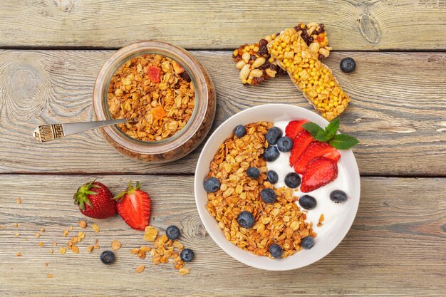 Tigela de granola caseira com iogurte e frutas frescas na superfície de madeira