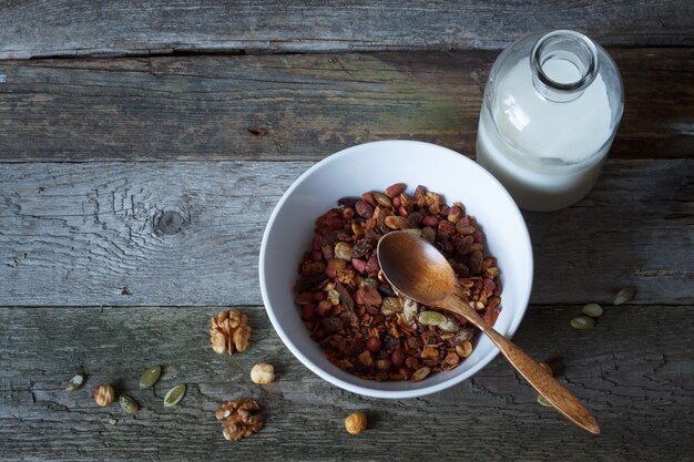 Tigela de granola de mel crocante com sementes de linho, cranberries e uma garrafa de leite em uma mesa