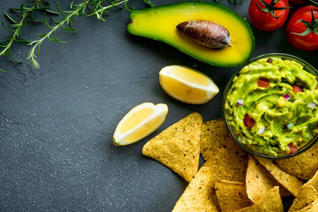 Foto tigela de guacamole com ingredientes e chips de tortilha em uma mesa de pedra. imagem de vista superior. copyspace para seu texto.