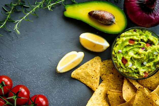 Foto tigela de guacamole com ingredientes e chips de tortilha em uma mesa de pedra. imagem de vista superior. copyspace para seu texto.