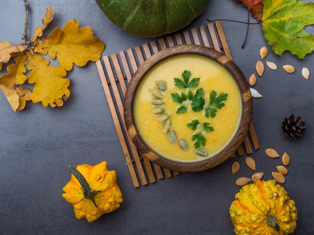 Tigela de madeira de sopa de abóbora tradicional na mesa cinza decorada com sementes salsa folhagem colorida abóbora decorativa