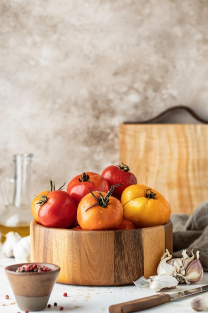 Tigela de madeira de tomates coloridos com garrafa de óleo de placa de faca de alho e pimenta com espaço de cópia