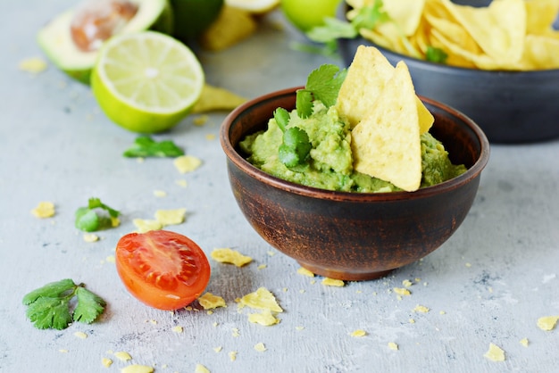 Foto tigela de mergulho de guacamole com nachos de milho (chips) e ingredientes em um fundo azul, foco seletivo. prato nacional mexicano.