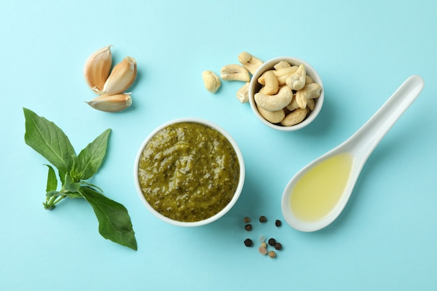 Tigela de molho pesto e ingredientes em fundo azul