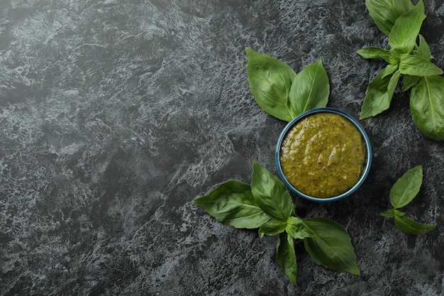 Foto tigela de molho pesto e manjericão em fundo preto esfumaçado