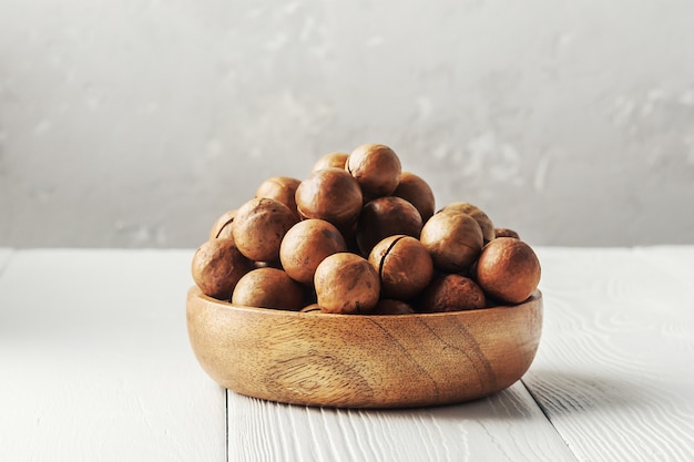 Tigela de nozes de macadâmia em uma mesa de madeira branca.