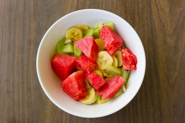 Tigela de salada de frutas deliciosa e saudável no café da manhã. Sobremesa em fundo de madeira