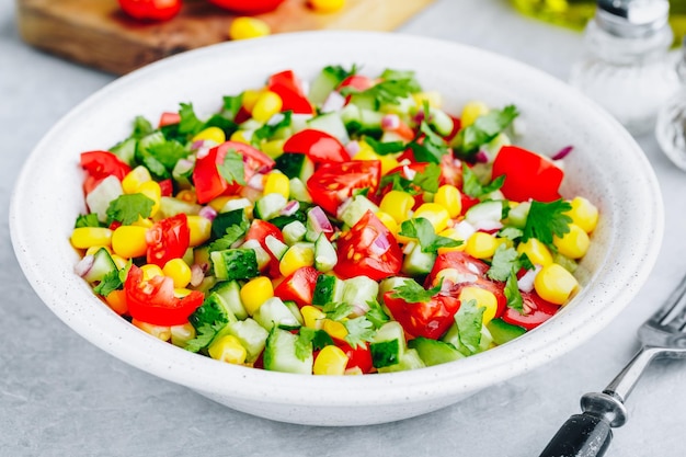 Tigela de salada de milho doce de verão fresco com tomates pepinos cebolas vermelhas e salsa