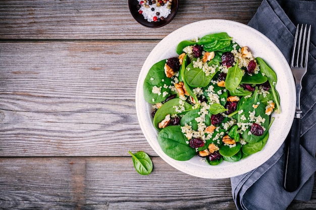 Tigela de salada verde com nozes de quinoa espinafre e cranberries secas em fundo de madeira