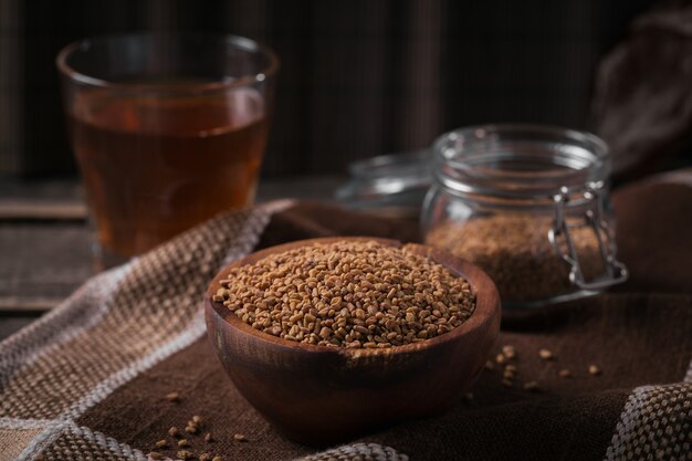 Tigela de sementes de feno-grego e chá amarelo de feno-grego egípcio ou bebida Methi Dana em fundo escuro de madeira