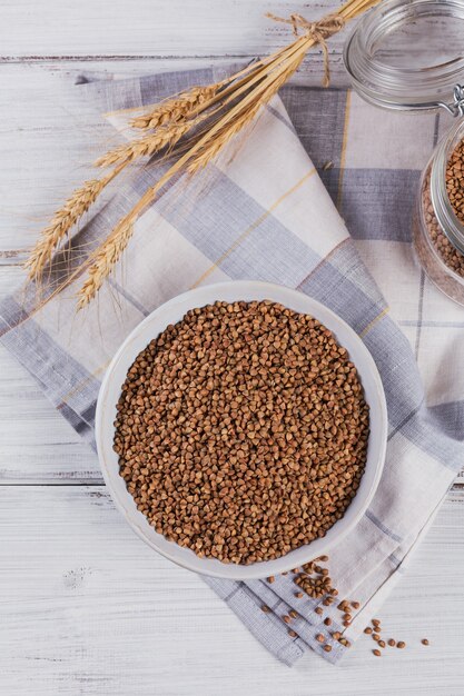 Tigela de sêmolas de trigo sarraceno crus secas em um fundo branco de madeira. Cozinhar o conceito de mingau de trigo sarraceno.