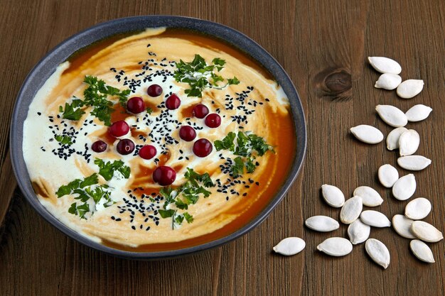 Tigela de sopa de abóbora cremosa com ervas de sementes de cominho preto creme e cranberries em uma mesa de madeira