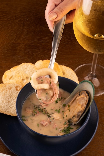 Tigela de sopa de frutos do mar com mexilhões torrados da Nova Zelândia e cebolinha em mesa de madeira close-up em cima retrato emparelhado com copo de vinho branco perder na colher com vista superior de lula e polvo