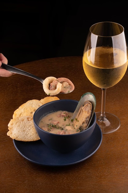 Tigela de sopa de frutos do mar com mexilhões torrados da Nova Zelândia e cebolinha em mesa de madeira close-up em cima retrato emparelhado com copo de vinho branco perdido em colher com retrato de lula e polvo