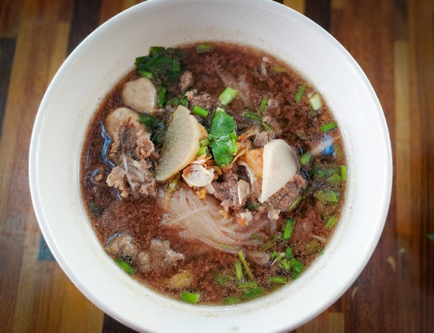 Tigela de sopa de macarrão de carne com bola de carne e vegetais no fundo da mesa de madeira